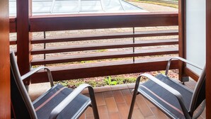 A covered outdoor area with a view of a multi-story building, a tiled patio, and two metal chairs. - Hotel Aquarell (Cegled)