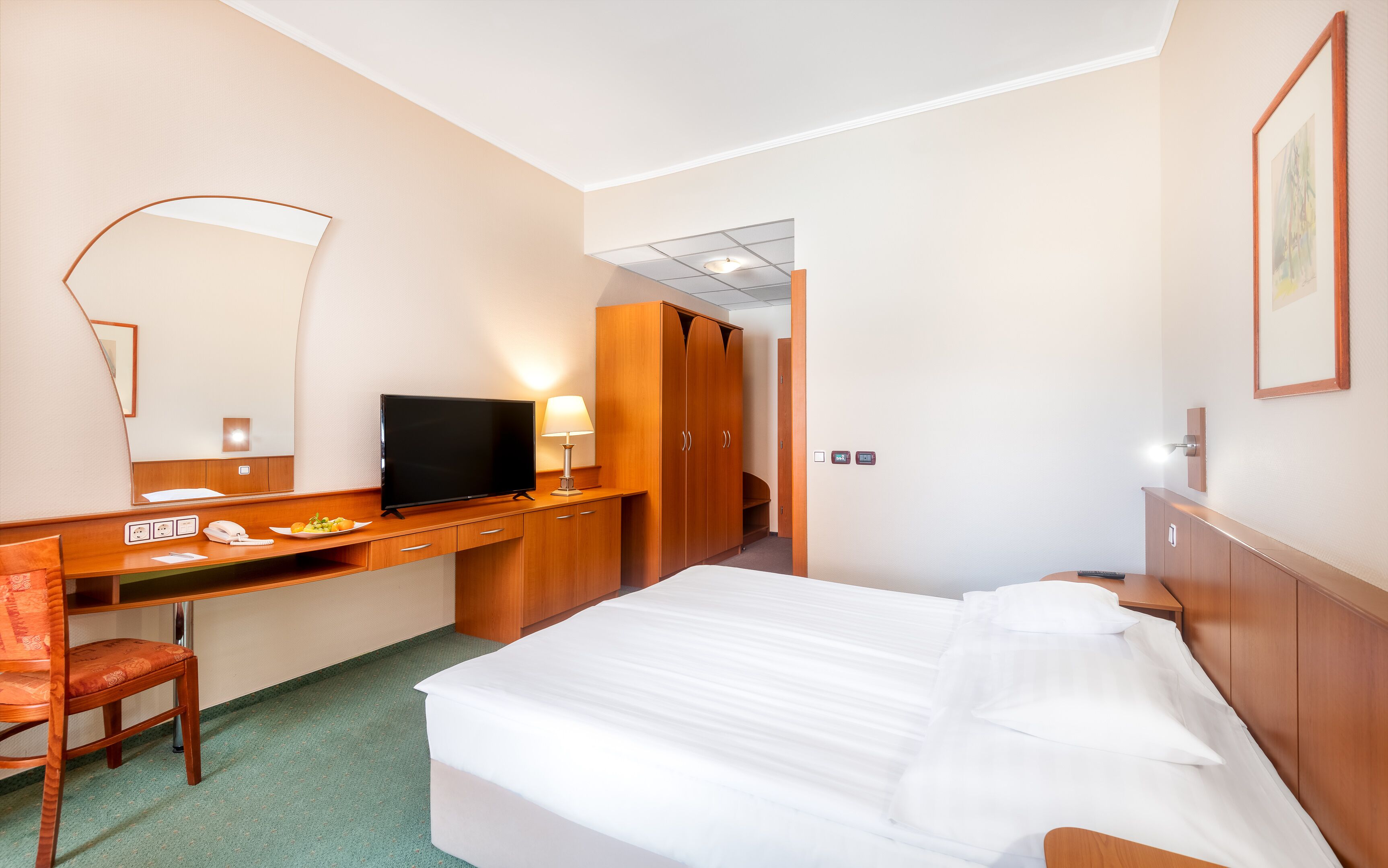 Quarto de hotel com cama, escrivaninha com telefone, televisão e espelho.