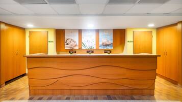 A reception area with a wooden reception desk, three framed posters on the wall, and wooden cabinets on either side.