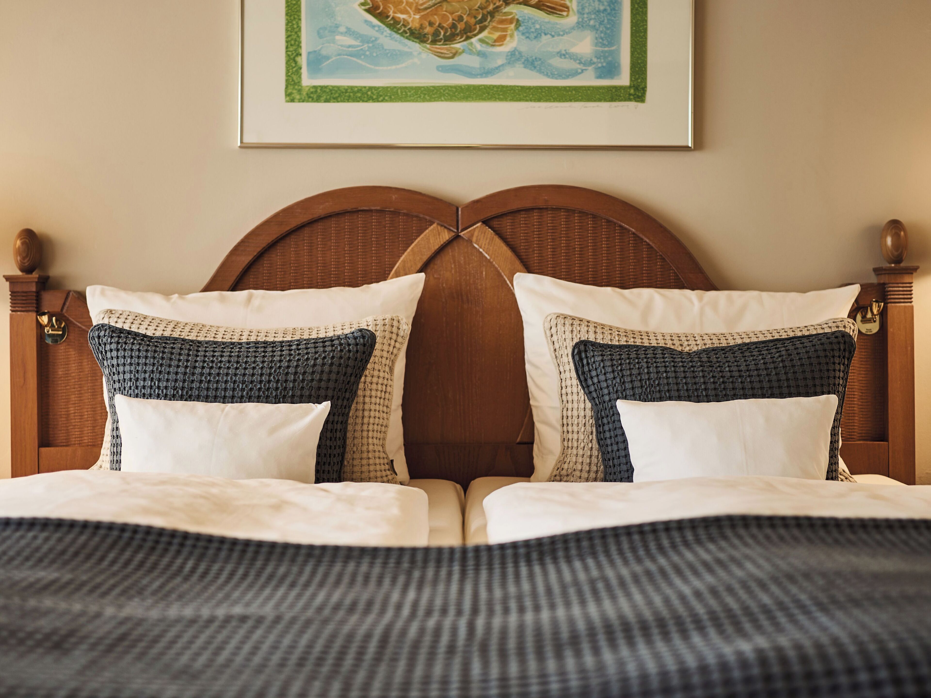 Una cama bien hecha con una colcha de cuadros, dos almohadas de diseño pata de gallo y una obra enmarcada encima.