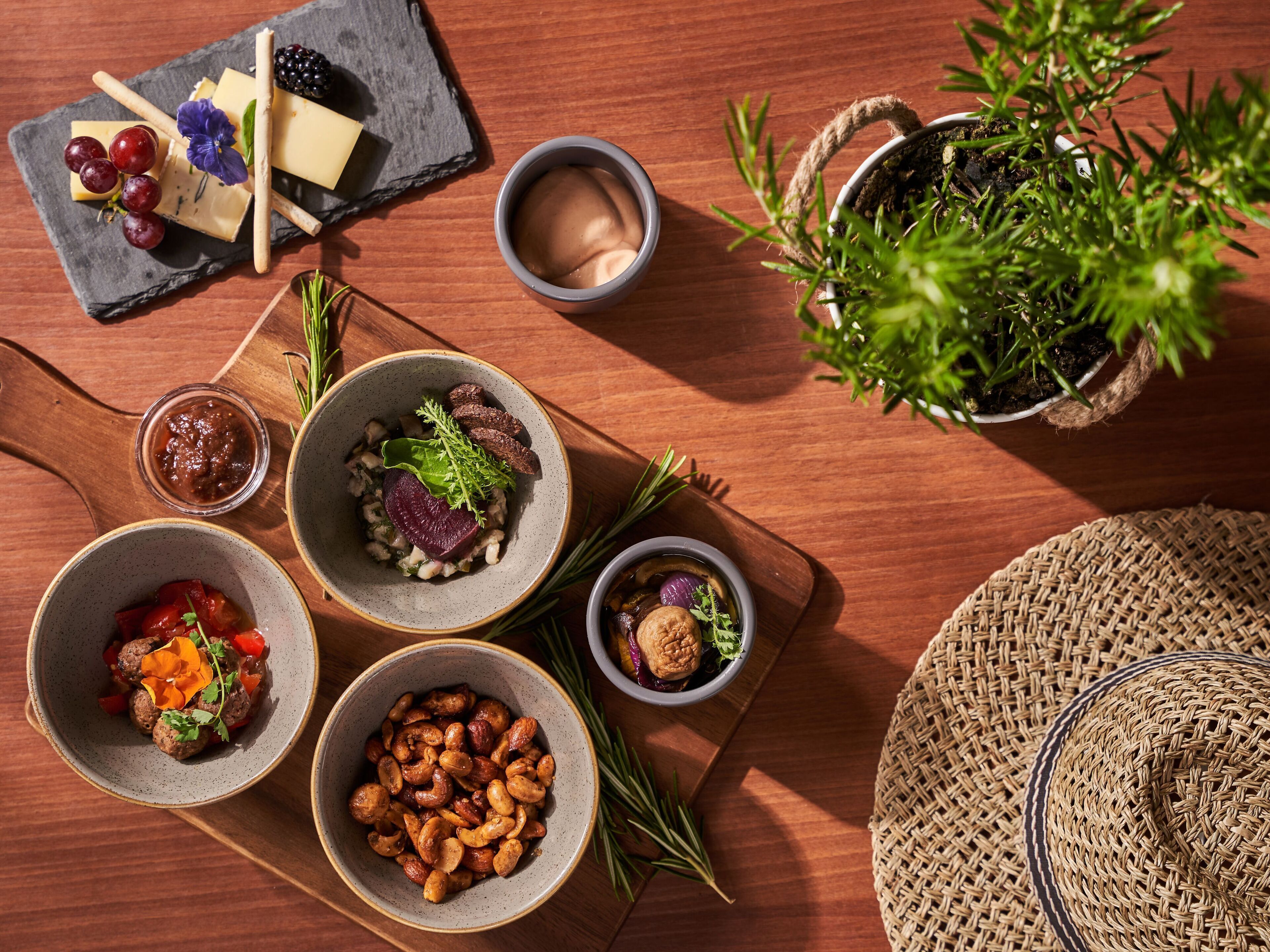 A wooden table with various food items, including bowls of nuts, meatballs, and a cheese board.