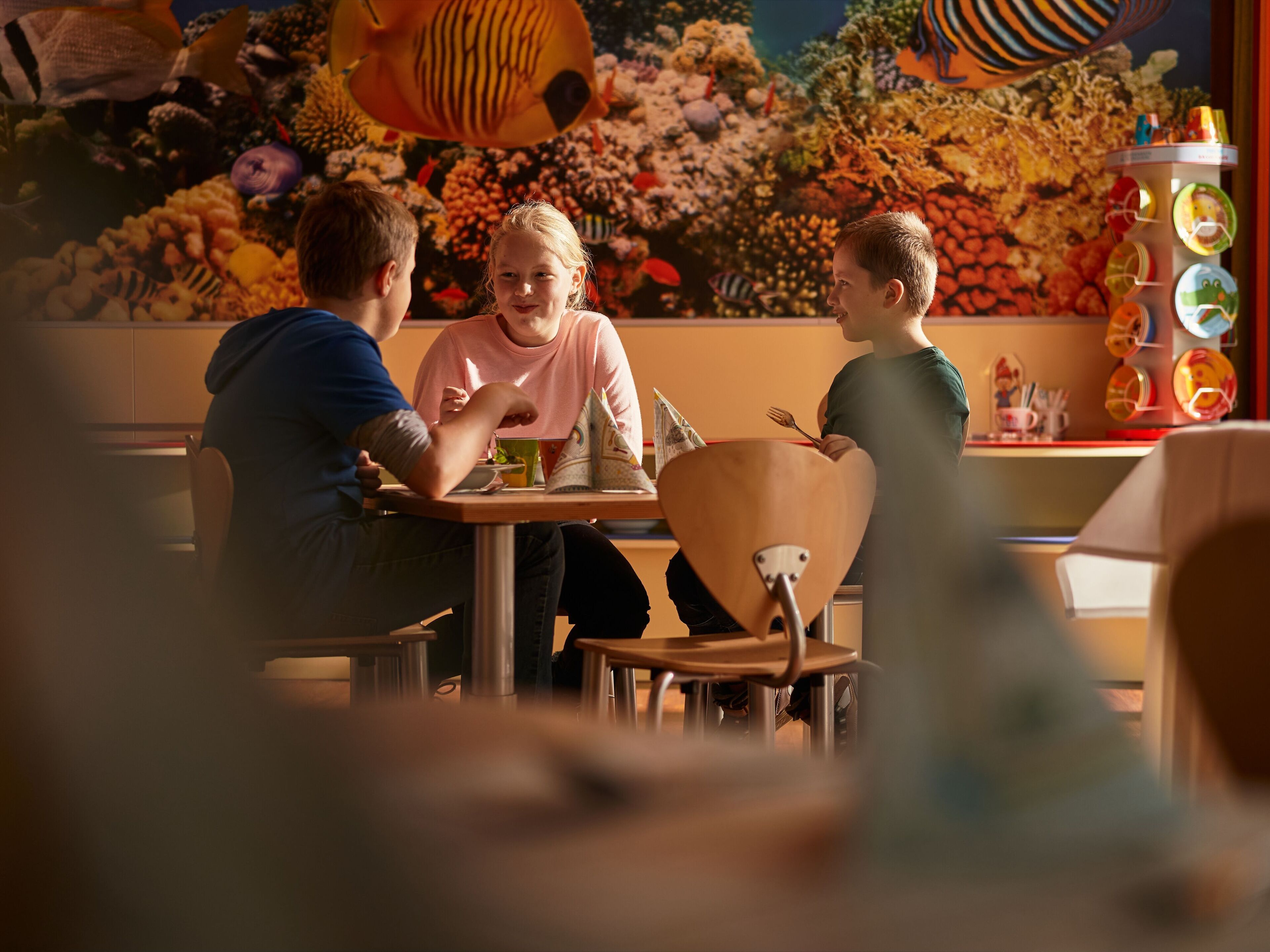Tre personer sitter vid ett bord på en restaurang, med en väggmålning med undervatentema i bakgrunden.