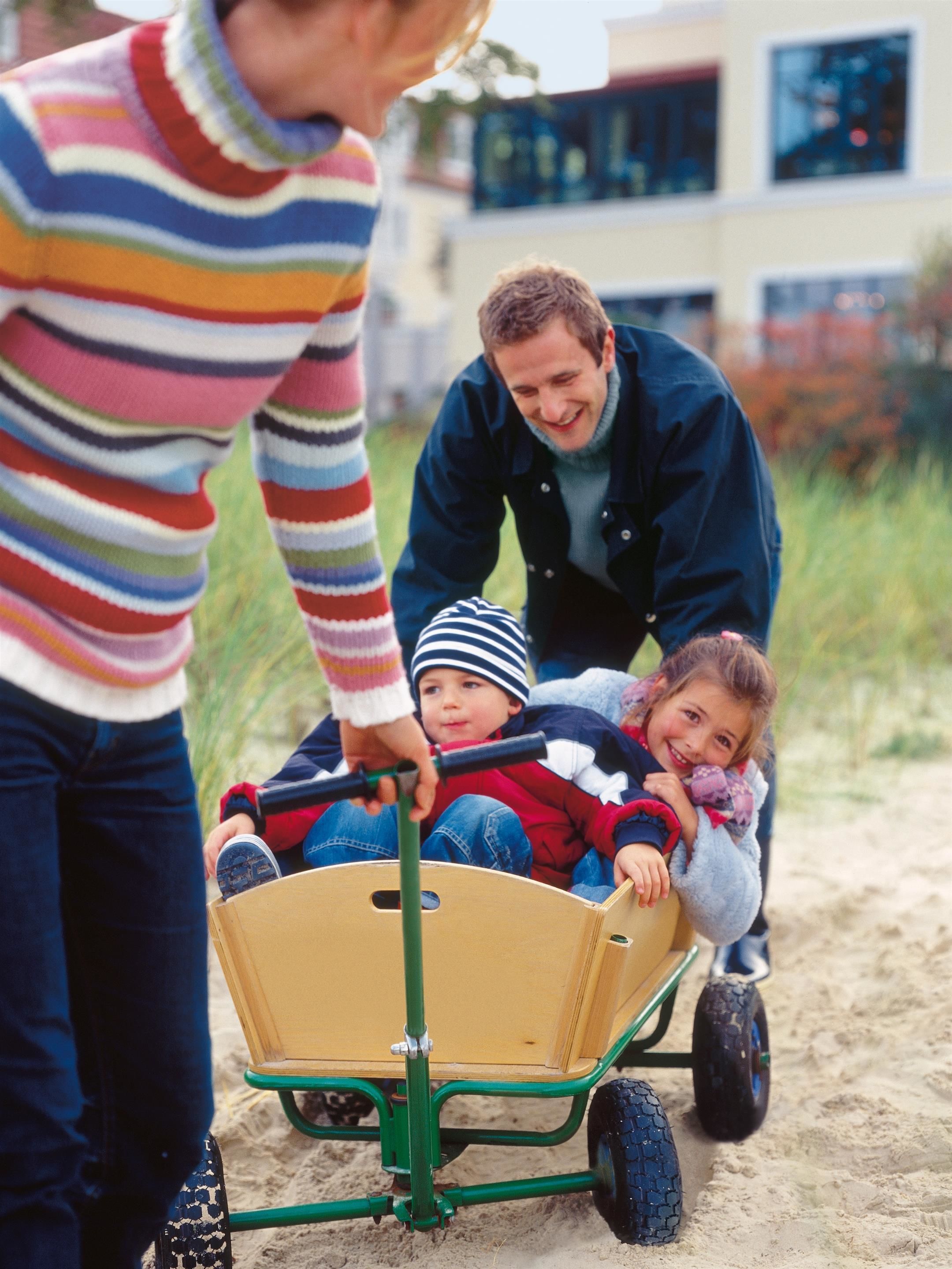 A family with a child in a wagon on a sandy surface, possibly a beach or park.