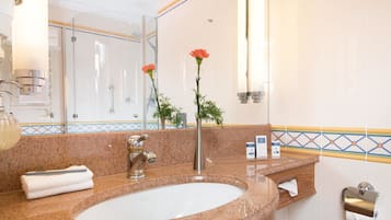 Un baño con lavamanos de encimera de granito, un espejo, una ducha y un florero con flores.