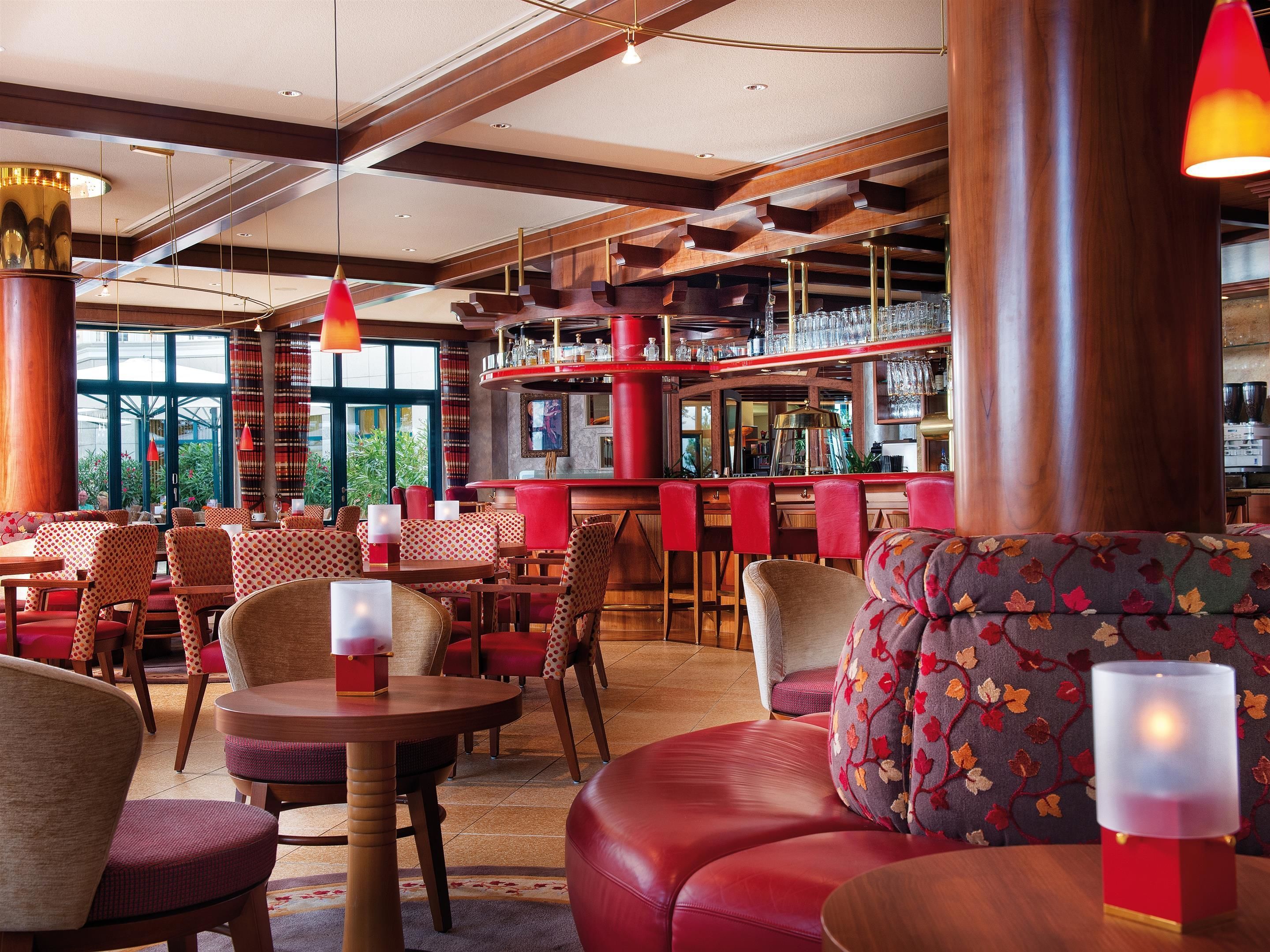 A bar area with multiple seating options, including round tables and cushioned booths, with a bar counter and shelves of glasses and bottles.