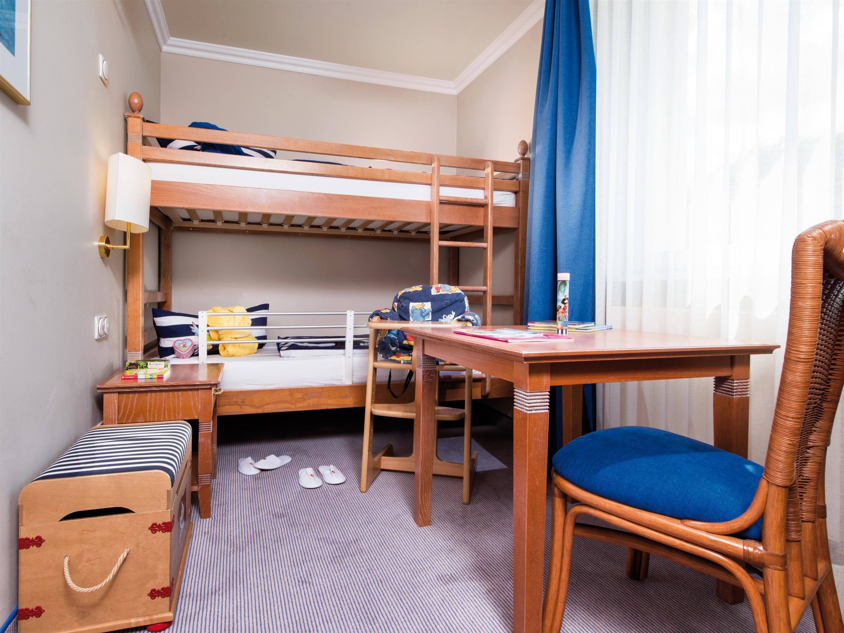 A bunk bed room with a desk, chair, and a suitcase.