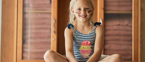 A child sitting on a bed in a room with wooden furniture and a cabinet.
