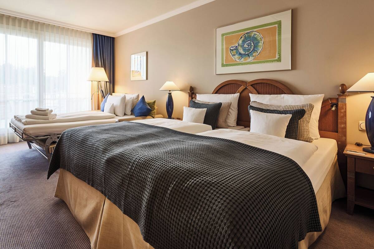 Habitación de hotel con una cama grande, dos mesitas de noche, una ventana con cortinas y una obra de arte enmarcada en la pared.