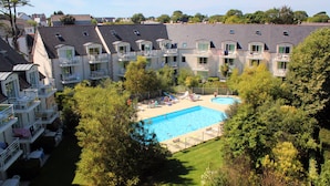 A hotel with a swimming pool surrounded by lush greenery and multiple balconies. - Résidence Le Domaine des Glénan (Fouesnant)