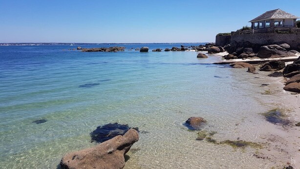 A coastal view with clear water, rocks, and a small building with a thatched roof. - Résidence Le Domaine des Glénan (Fouesnant)