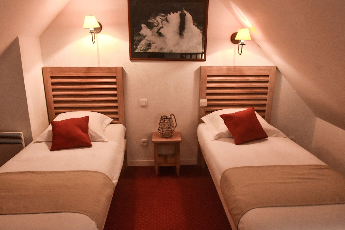 A hotel room with two single beds, each with a red pillow, a small wooden nightstand, and a wall-mounted lamp.