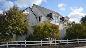 A two-story house with a balcony, surrounded by trees and a white fence. - Résidence Le Domaine des Glénan (Fouesnant)