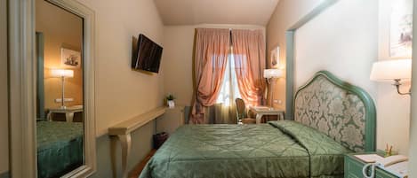 A bedroom with a bed, a desk, a chair, a TV, and a window with curtains.