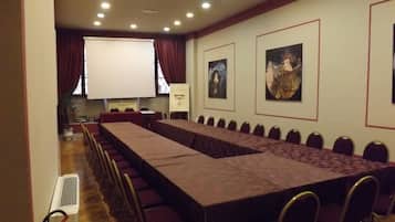 Un salón de conferencias con una larga mesa, sillas, una pantalla de proyector y cuadros en las paredes.
