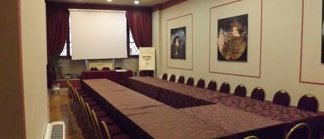A conference room with a long table, chairs, a projector screen, and framed artwork on the walls.