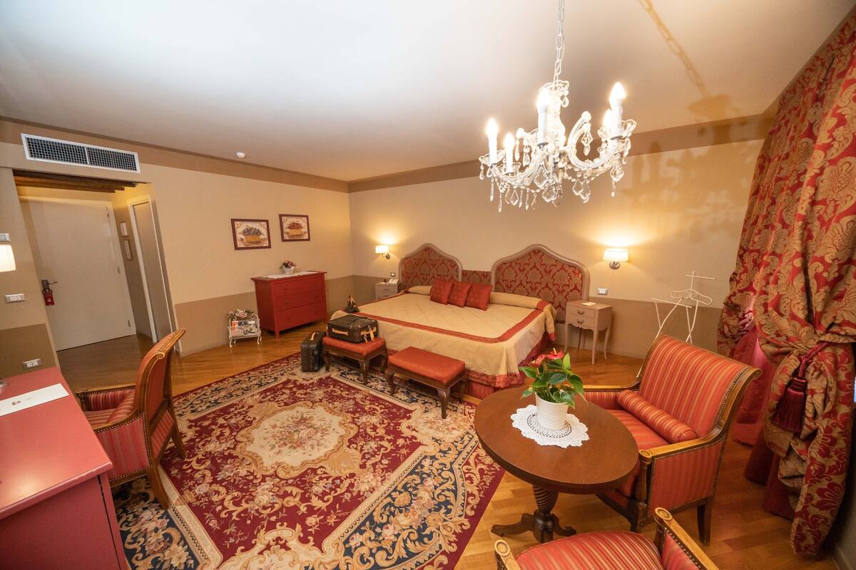 A spacious bedroom with a large bed, a chandelier, a dining table, and a red patterned sofa.