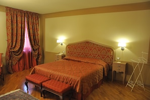 A hotel room with a large bed, two bedside tables, a nightstand, a bench, and a wardrobe.
