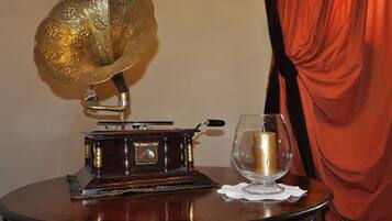 Ein Grammophon aus vergangenen Zeiten auf einem Holztisch neben einem Glas mit Kerze, vor einem roten Vorhang und einer schlichten Wand.