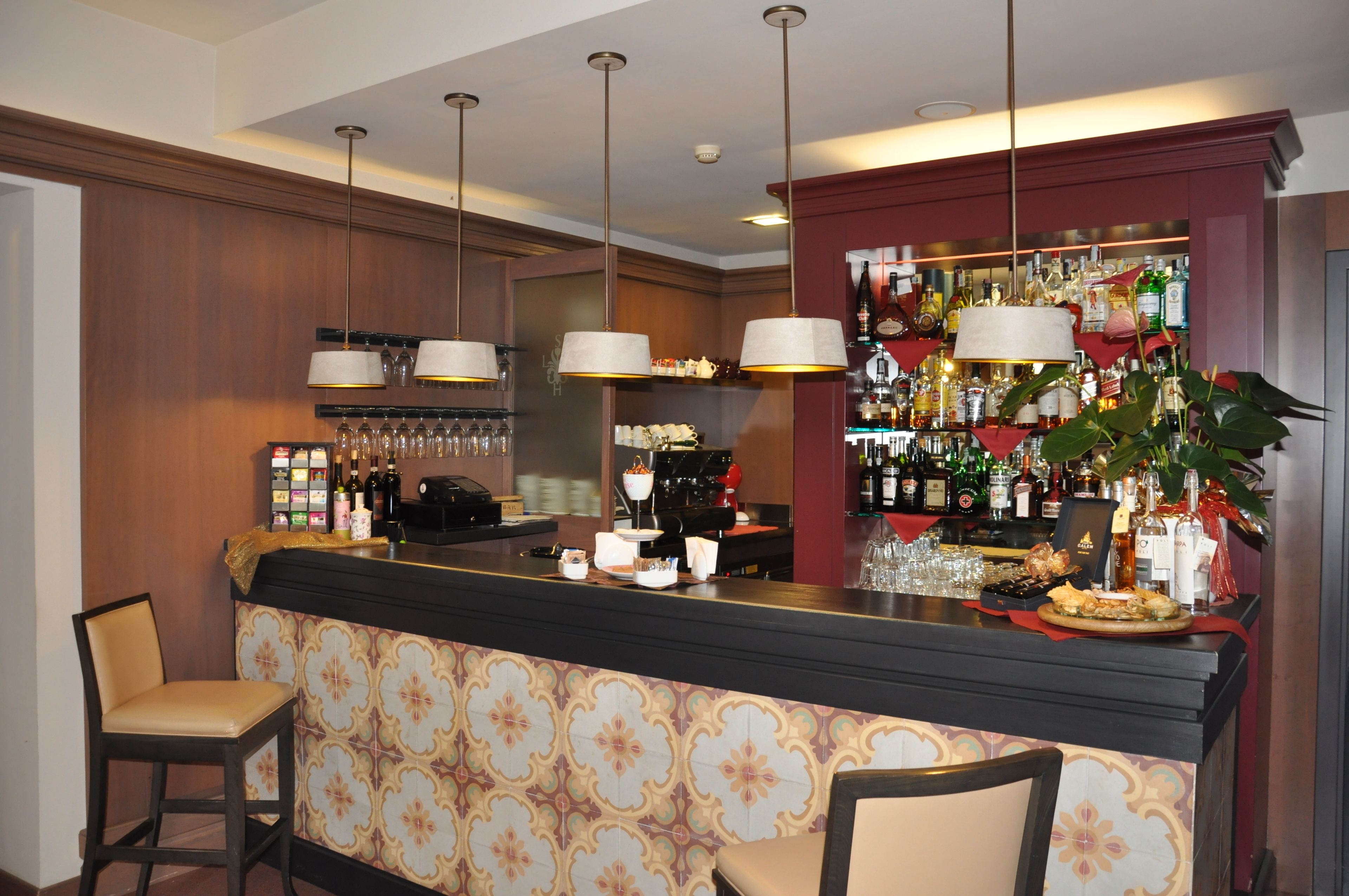 Zona de bar con pared decorada, lámparas colgantes y varios botellas y vasos en estantes.