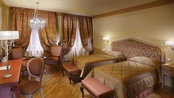 Quarto de hotel com duas camas, uma escrivaninha com luminária, uma cadeira e um candelabro.