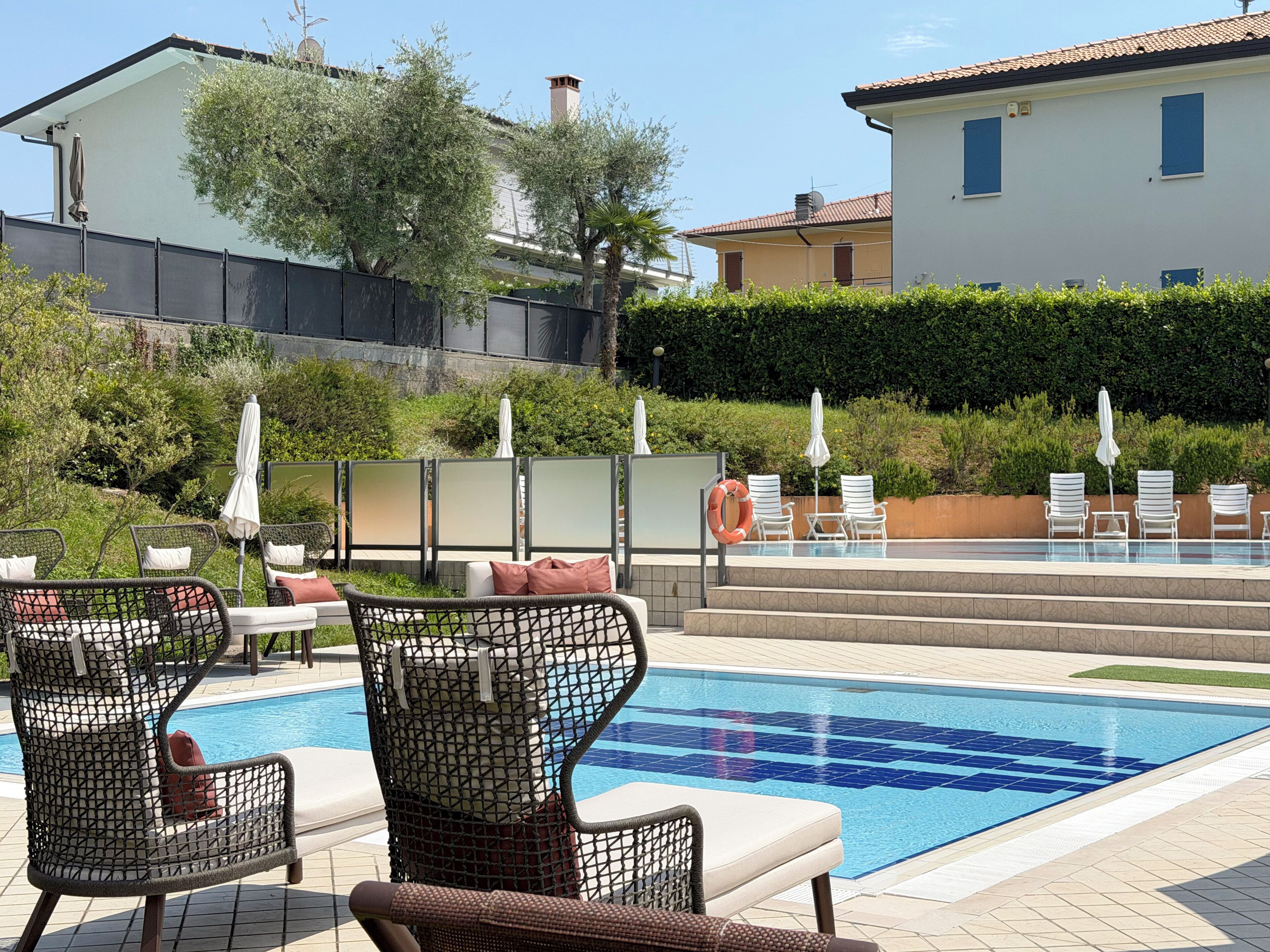 A swimming pool with lounge chairs and umbrellas, surrounded by greenery and buildings.