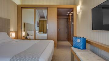 A hotel room with a large bed, a bedside table with a lamp, a blue bag on a bench, and a TV mounted on the wall.