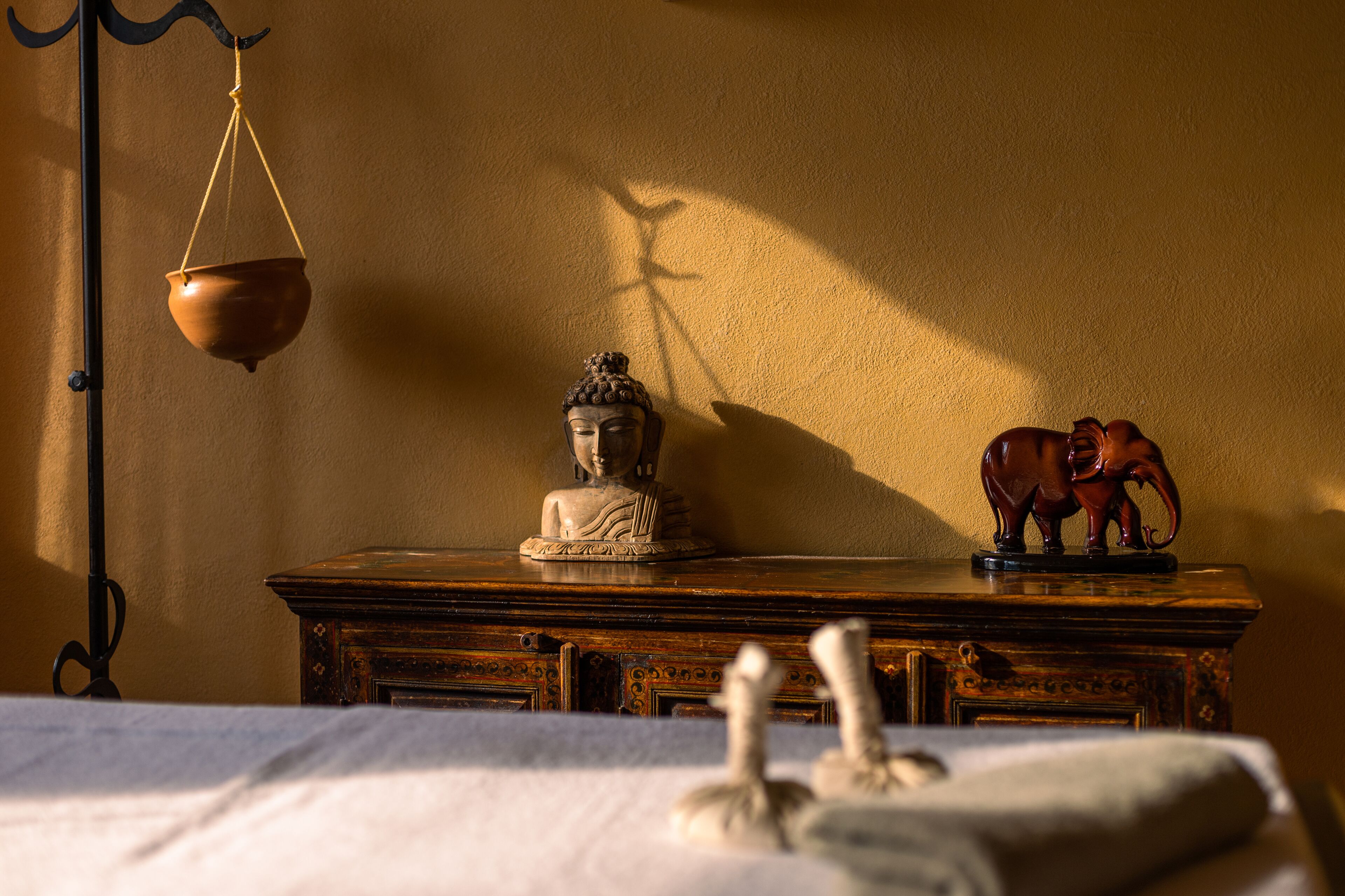 A statue of Buddha on a wooden table with a hanging pot and an elephant figurine.