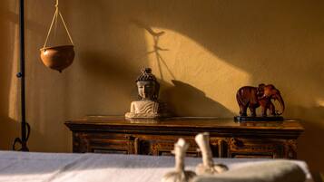 A statue of Buddha on a wooden table with a hanging pot and an elephant figurine.