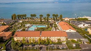 A coastal hotel with a swimming pool, a parking area, and a view of the sea.