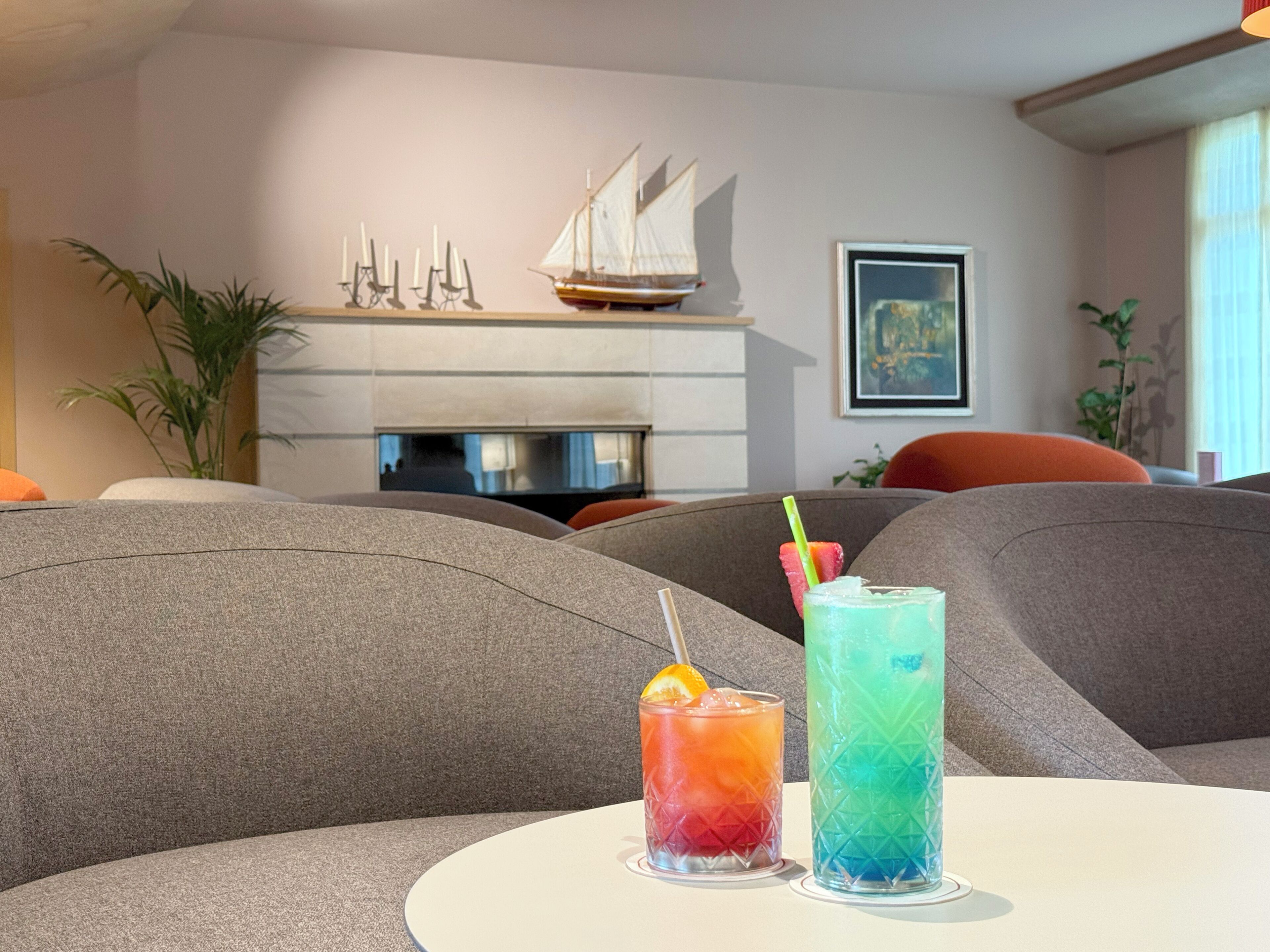 Una sala de estar moderna con chimenea, dos bebidas sobre una mesa y un modelo de velero en la repisa.