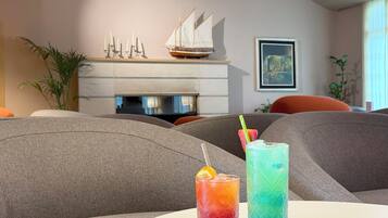 Una sala de estar moderna con chimenea, dos bebidas sobre una mesa y un modelo de velero en la repisa.