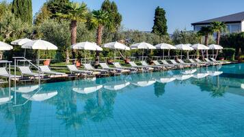 Ein Pool mit Liegestühlen und Sonnenschirmen, umgeben von Bäumen und einem Gebäude.
