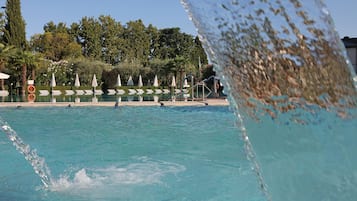 Een zwembad met helder water, omringd door ligbedden en parasols, met bomen op de achtergrond.
