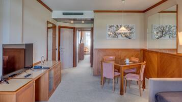 A compact hotel room with a kitchenette, a dining area with a table and chairs, a sofa, and a TV.