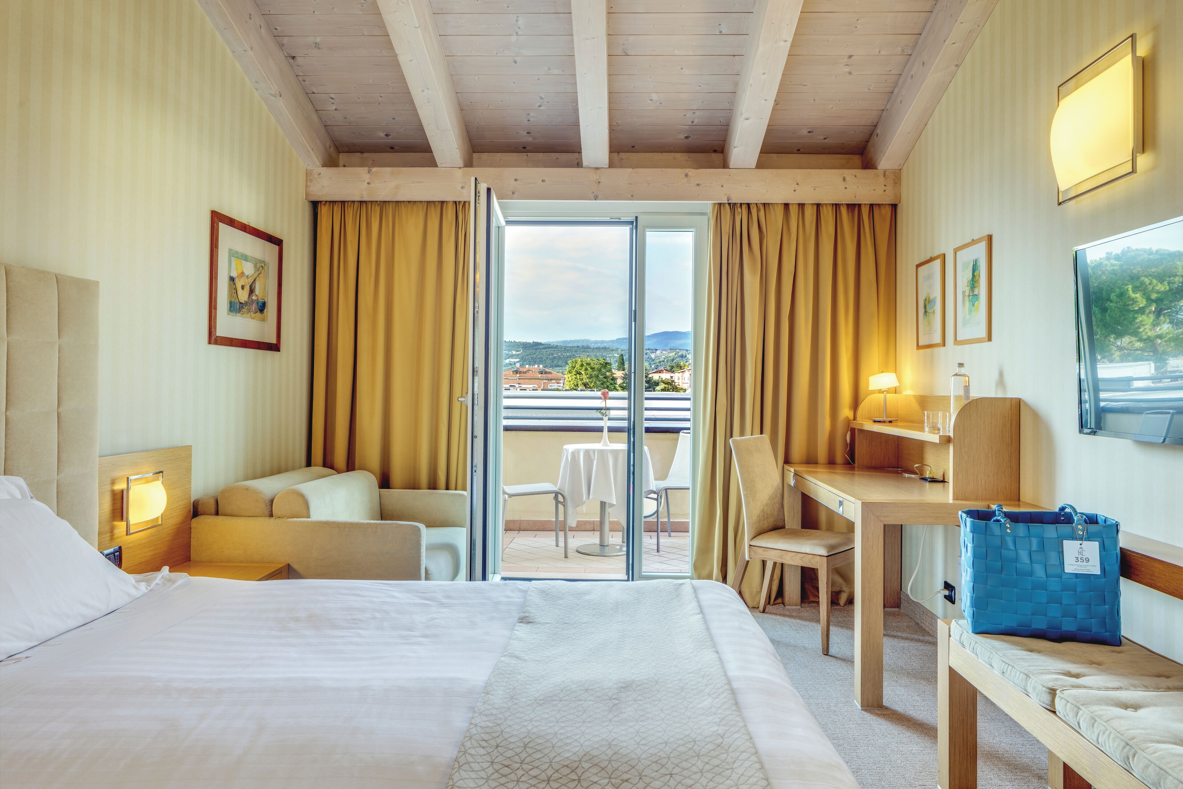 Una camera d'albergo con un letto, una scrivania, una sedia, un divano e un balcone con tavolo e sedie.