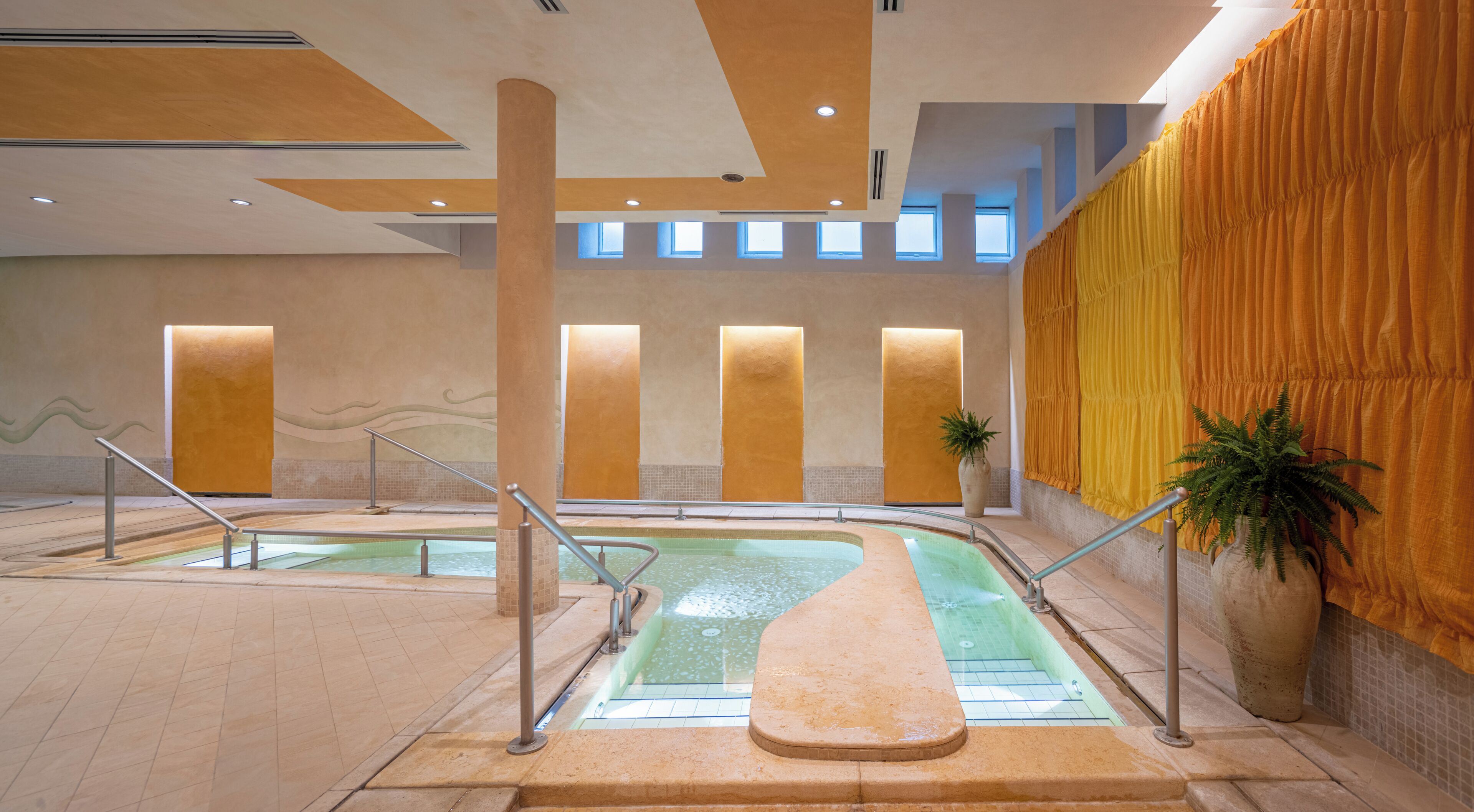 A pool area with two pools, a staircase, and a large potted plant.