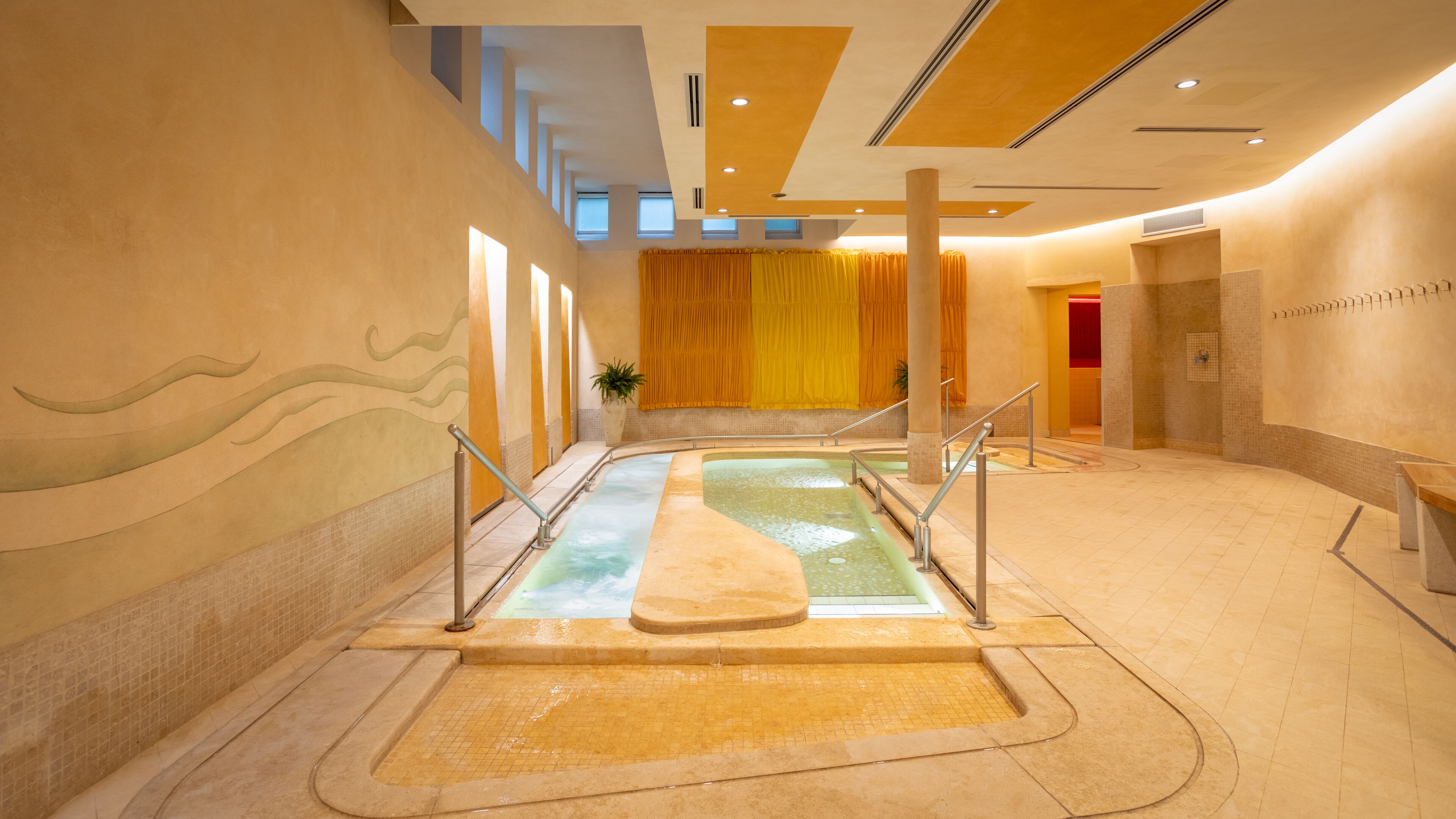 Zona de spa con una bañera de hidromasaje, suelo de baldosas y un fondo con cortina amarilla.
