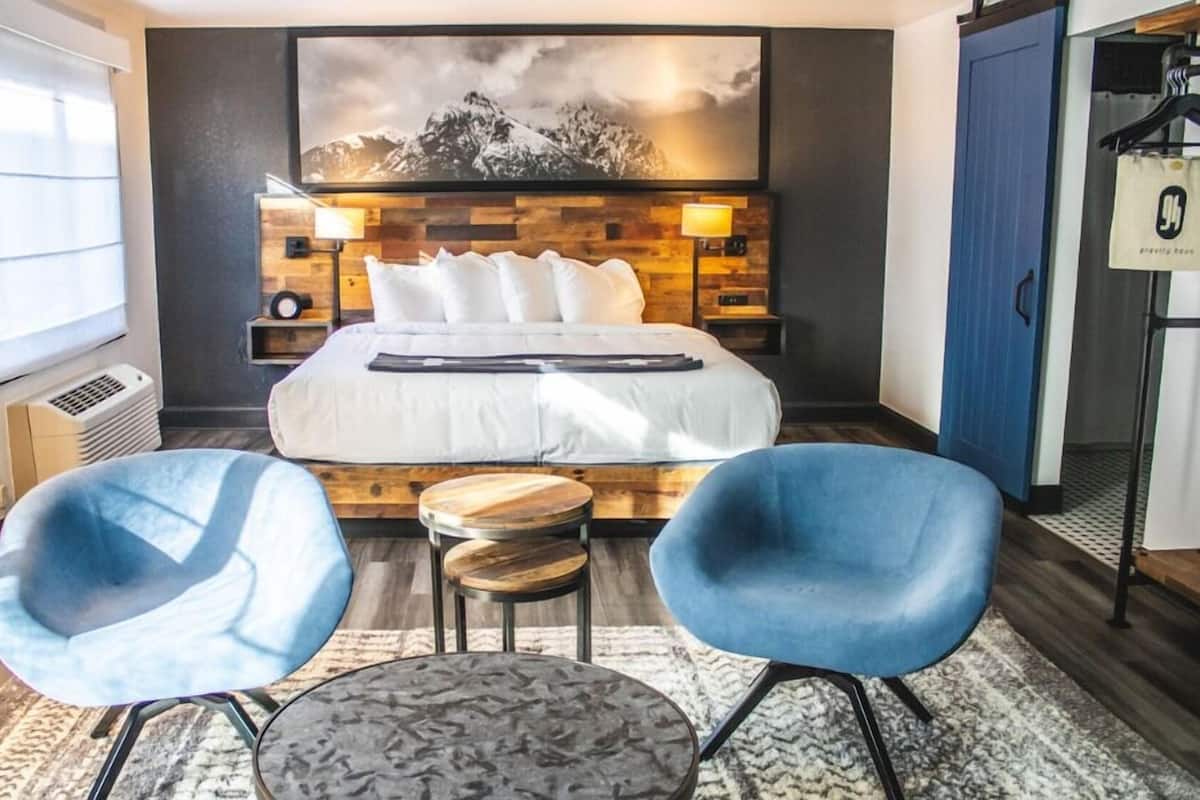 Ein Hotelzimmer mit einem Bett, zwei blauen Stühlen, einem kleinen Tisch, einer Wandlampe, einem Heizgerät und einem Bergpanorama.