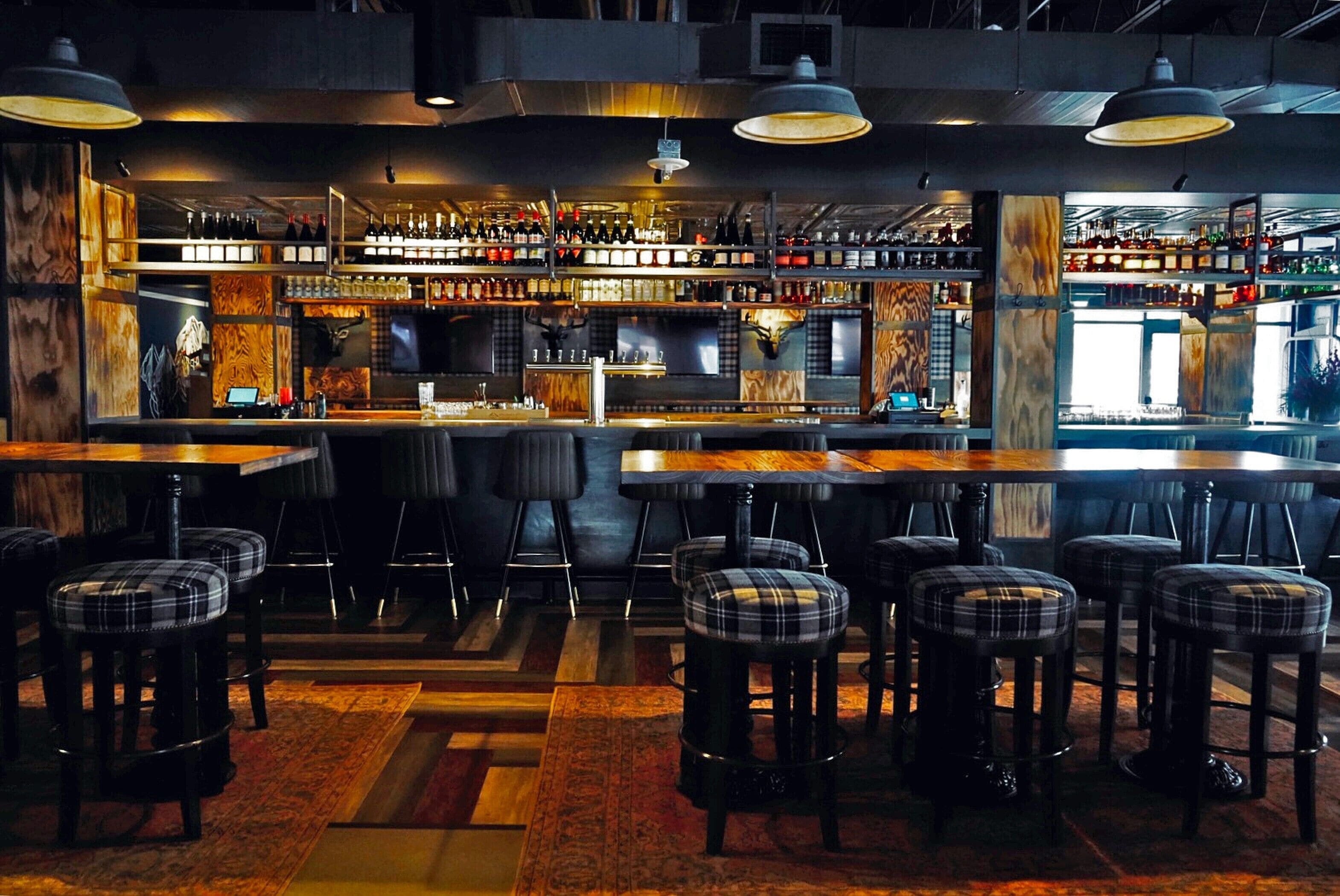 A bar area with multiple stools, a bar counter, and shelves stocked with bottles.