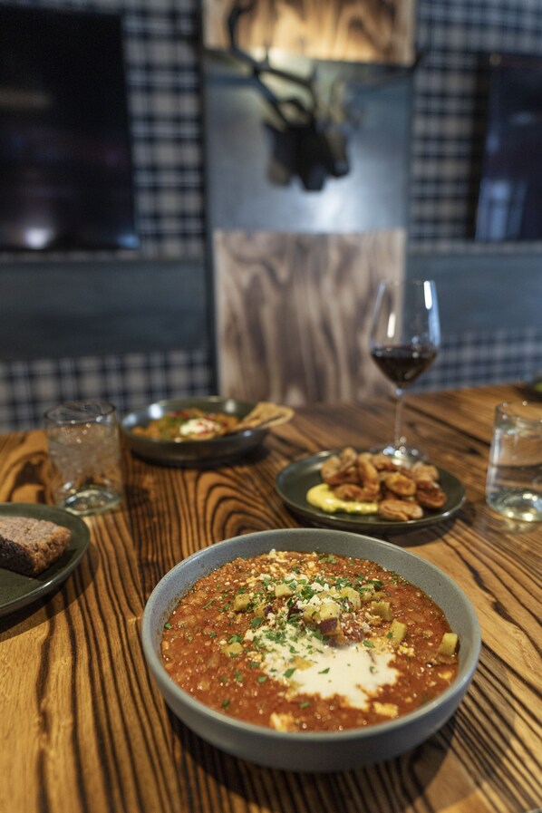 Una mesa de madera con un tazón de sopa, una copa de vino tinto y un plato de nueces.