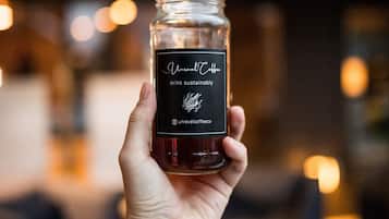 A hand holding a jar labeled "Unravelt Coffee" with a blurred background of a cafe interior.