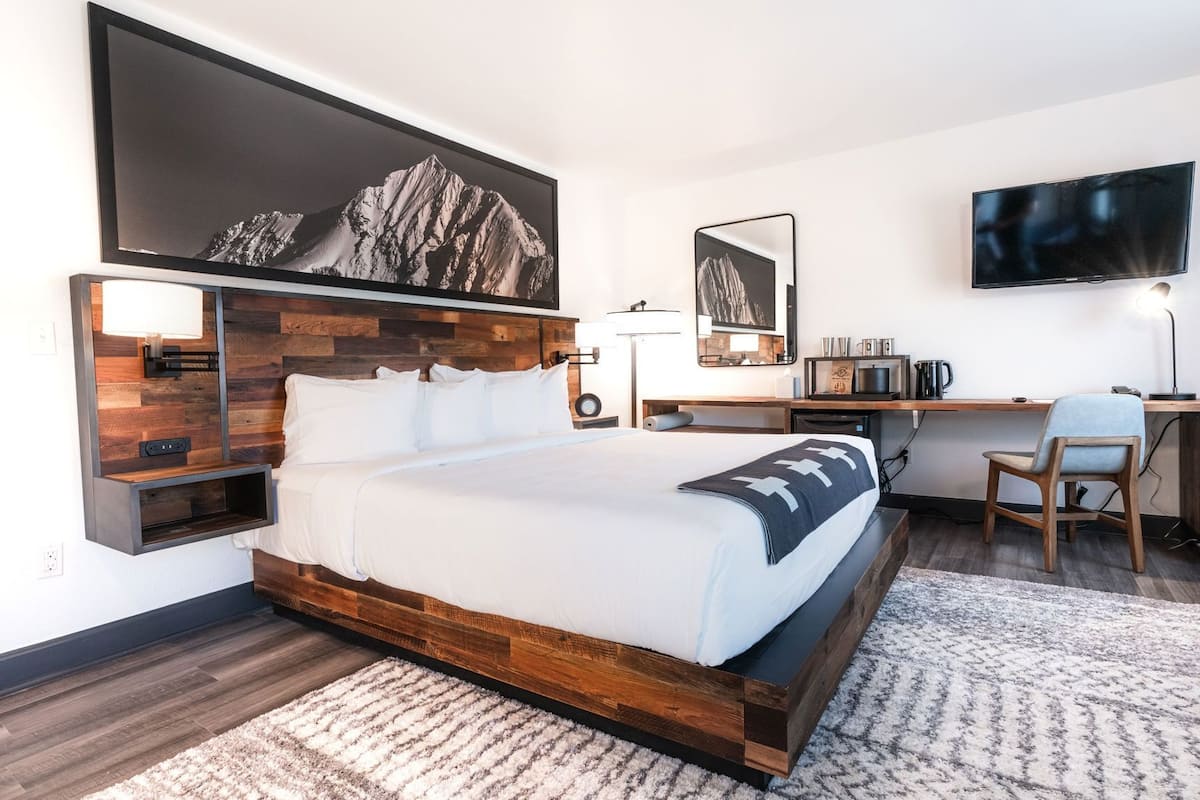 Ein modernes Hotelzimmer mit einem großen Bett, einem Schreibtisch, einem Flachbildfernseher und einem Berg-Kunstwerk an der Wand.