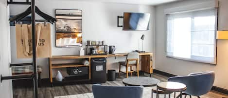 A modern hotel room with a desk, two chairs, a TV, and a large window.