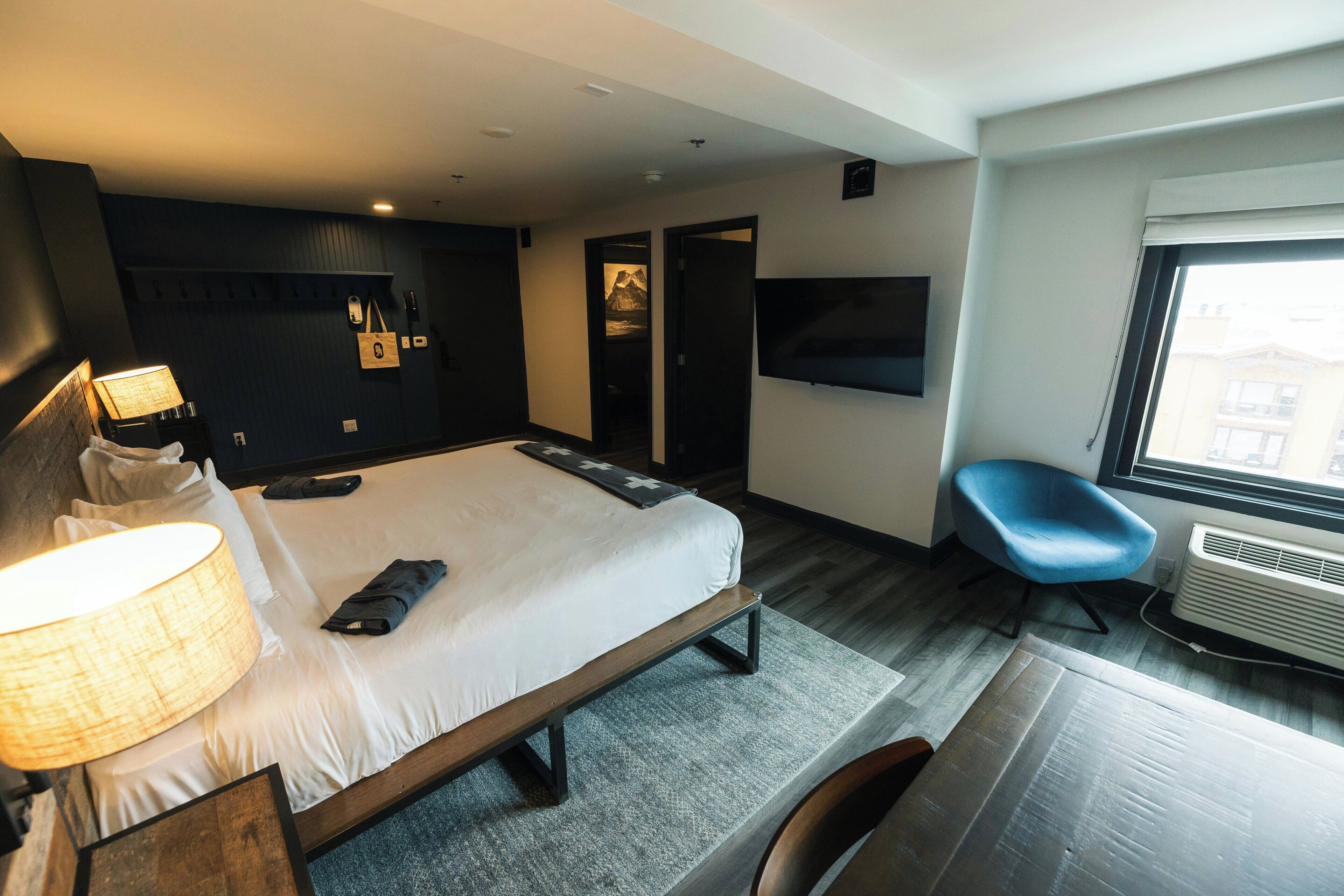 A hotel room with a bed, bedside lamp, flat-screen TV, chair, and a window.