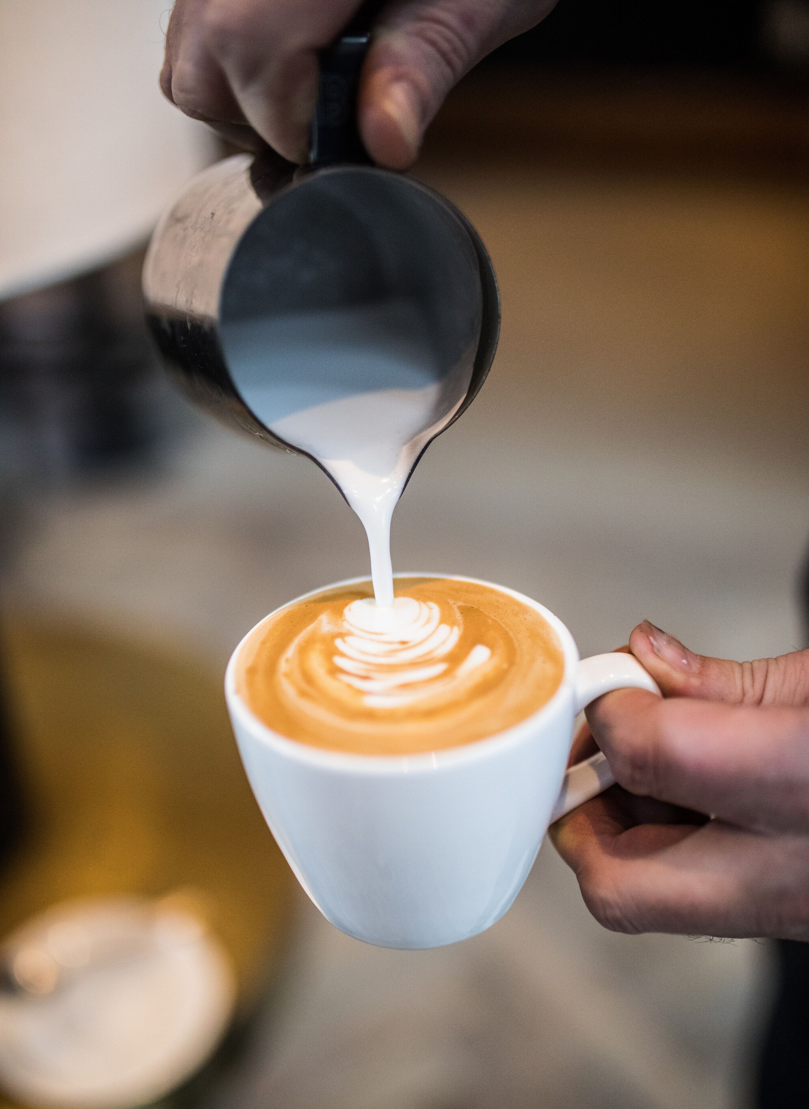 Une personne verse du lait dans une tasse de café, créant ainsi un motif artistique sur la mousse.