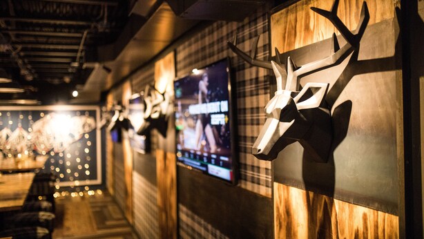 L’intérieur d’un restaurant avec des murs en bois, des têtes d’animaux empaillées accrochées aux murs et un écran de télévision diffusant un événement sportif.