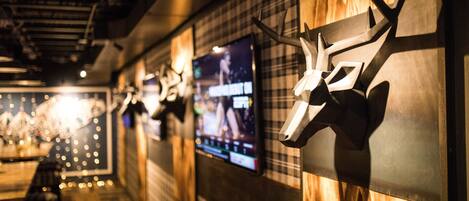 Interior de restaurante con paredes de madera, cabezas de animales montadas en la pared y una pantalla mostrando un evento deportivo.