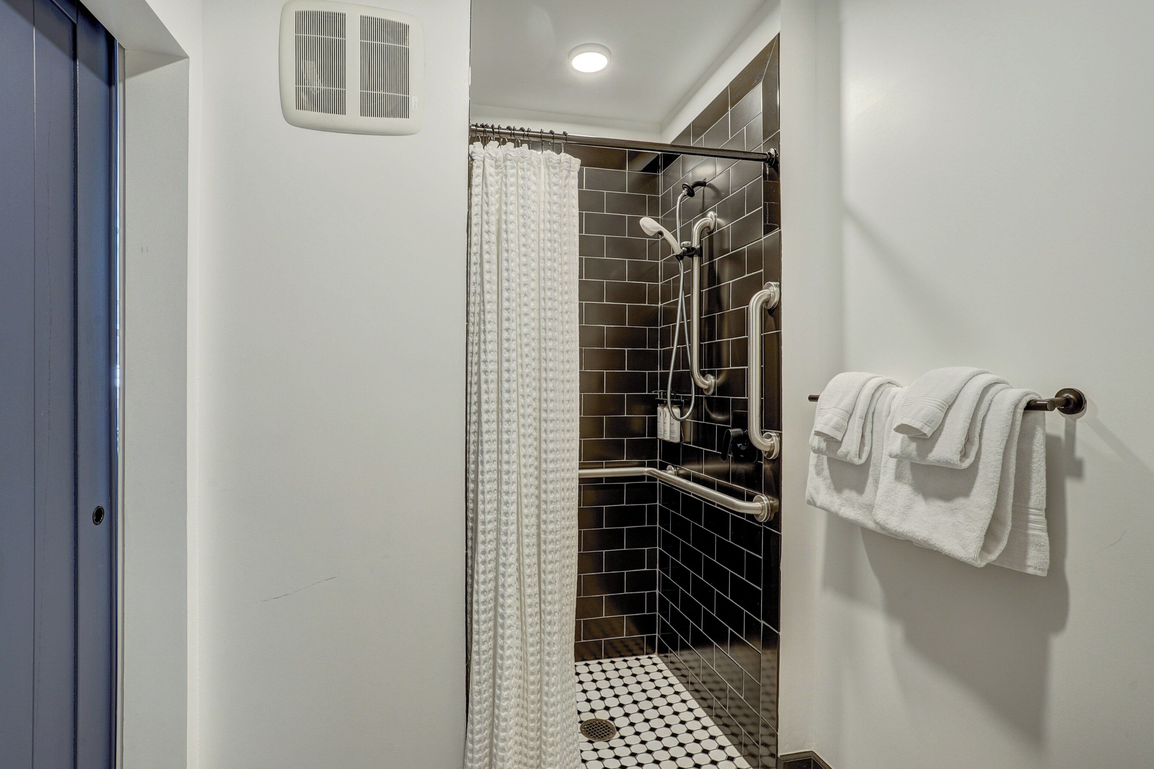 A bathroom with a shower, tiled walls, a towel rack, and a door.