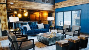 A modern lounge area with a blue sofa, armchairs, a coffee table, and a large window offering a view. - Gravity Haus Breckenridge (Breckenridge)