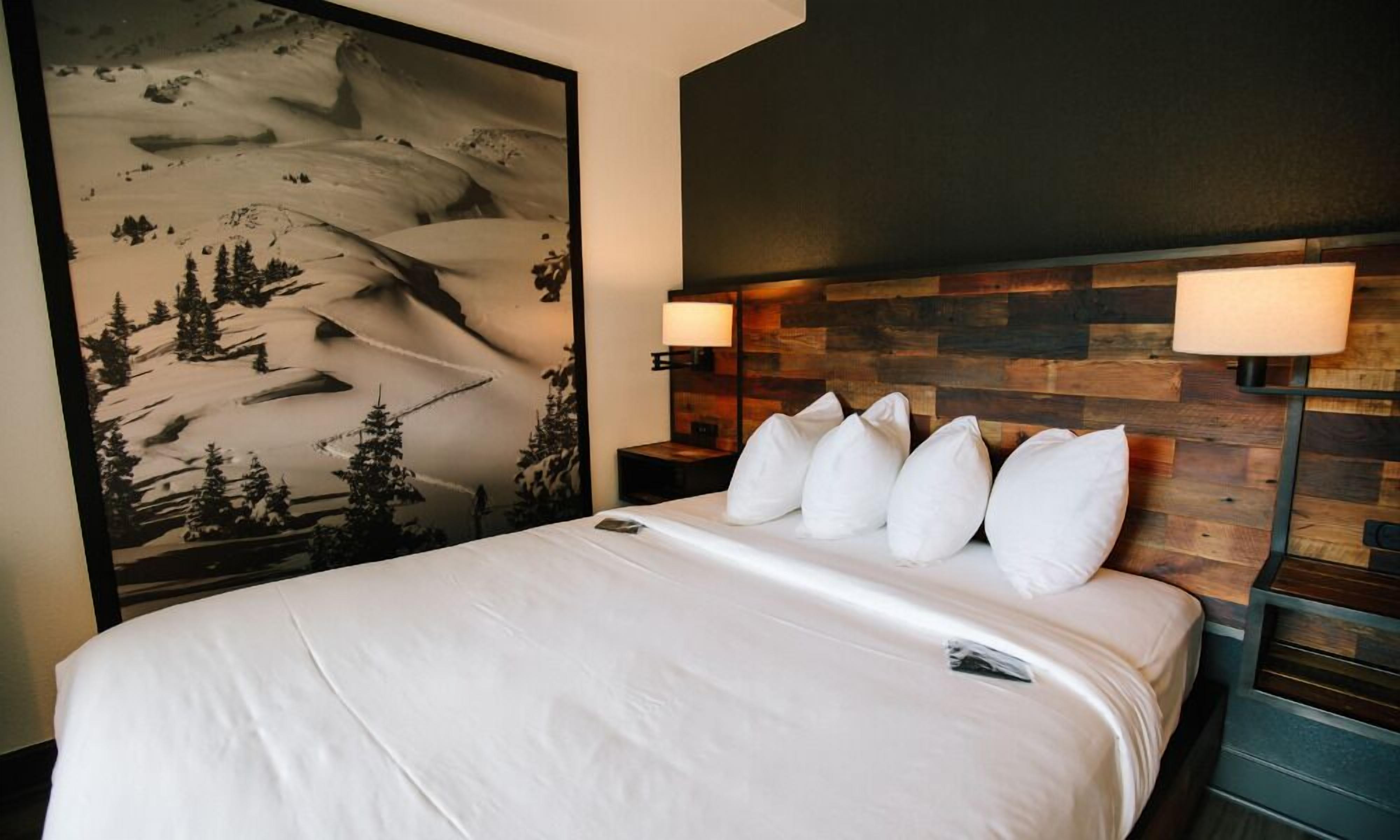 Habitación de hotel con una cama grande, un cabecero de madera y un mural en la pared que muestra un paisaje de montaña nevada.